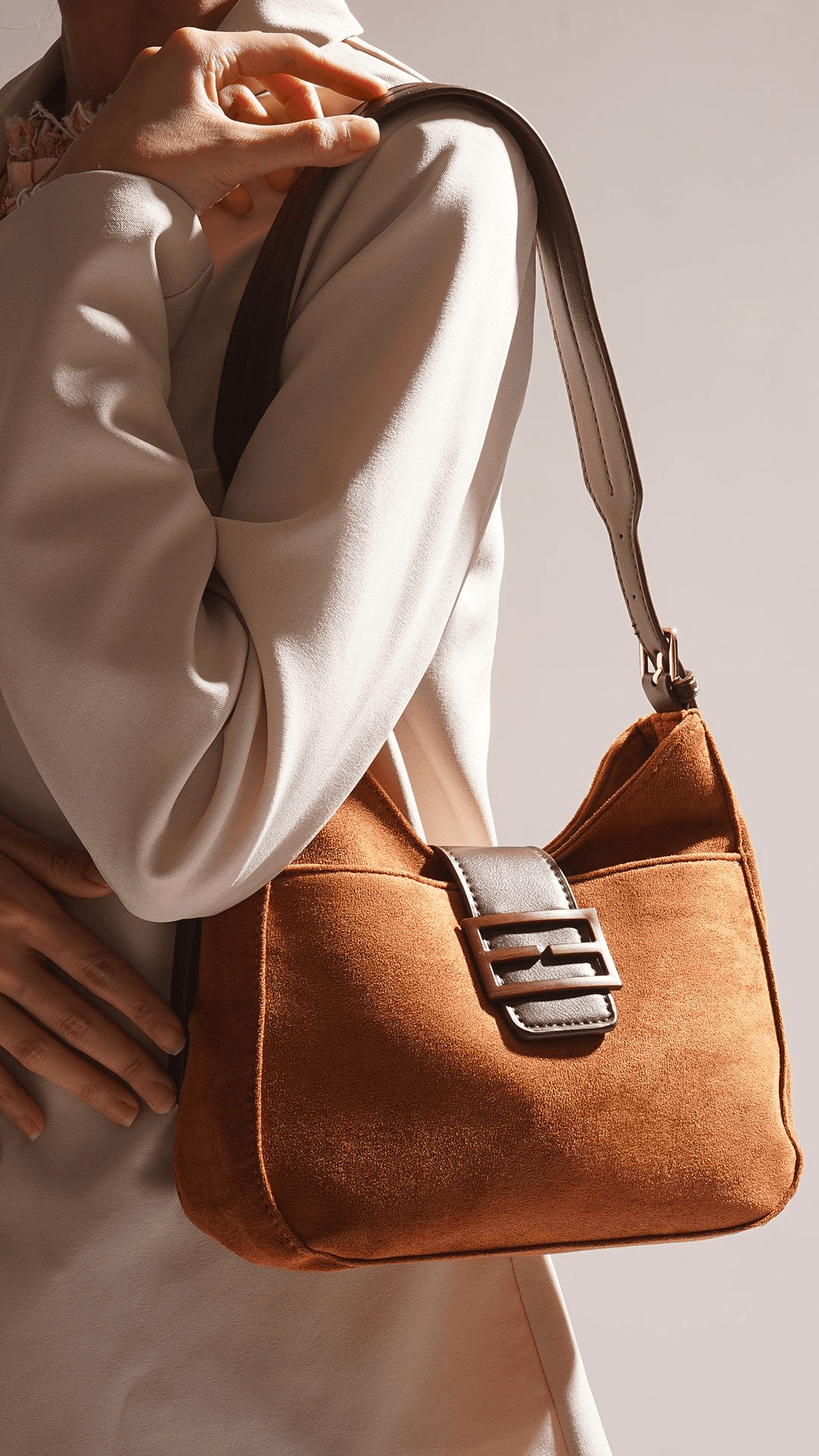Close crop of a suede shoulder bag worn against a knit sleeve