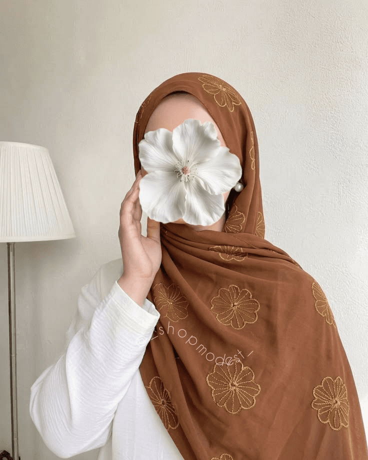 Model in a brown embroidered hijab holding a white flower
