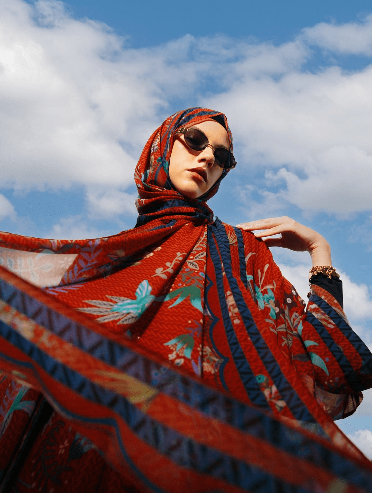 Model in a printed silk hijab catching the wind against a blue sky